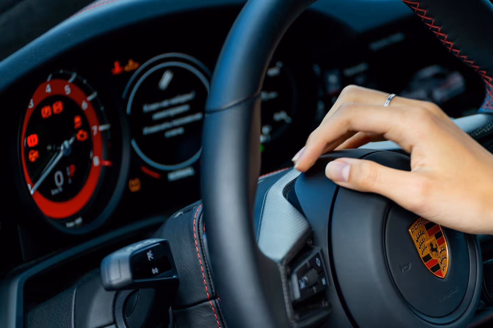 A hand on a Porsche steering wheel.