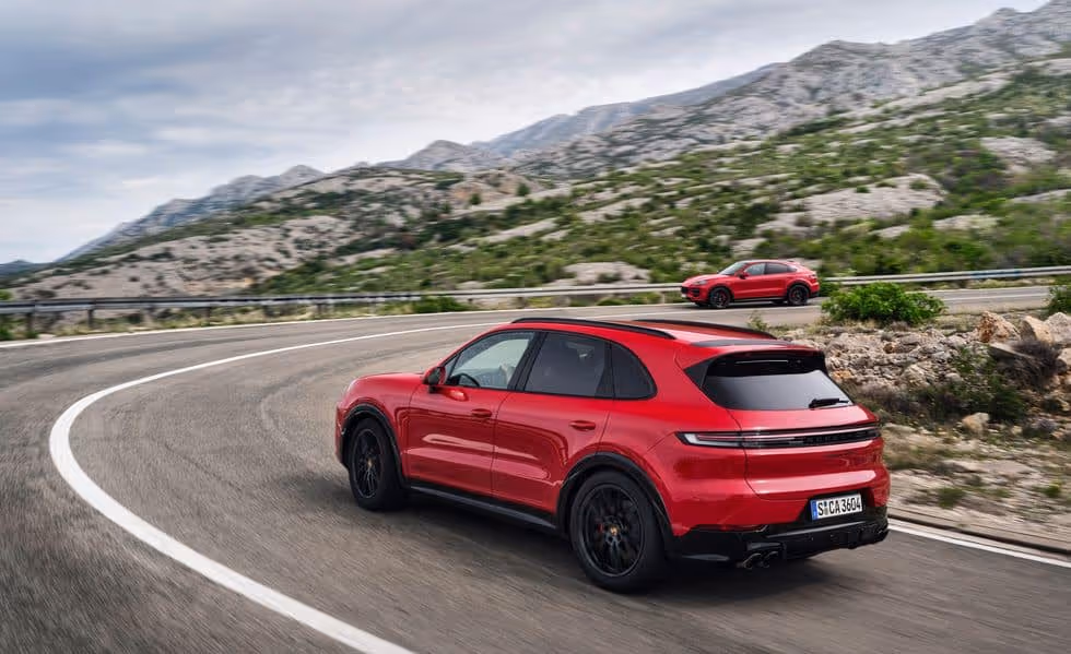 A red Porsche Cayenne GTS driving in a mountain slope.